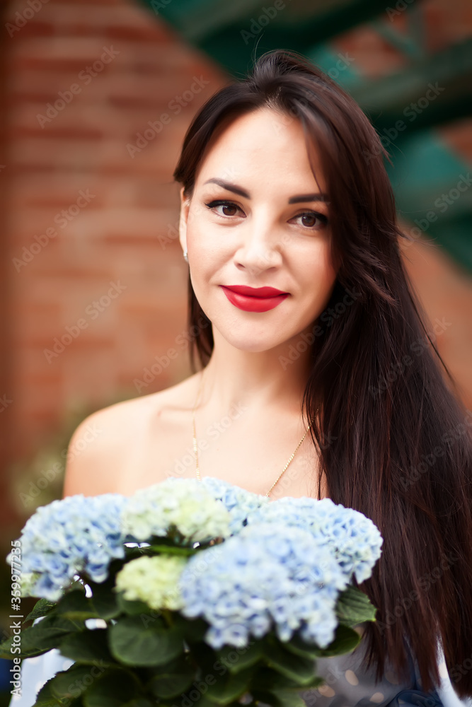 Beautiful brunette woman in a blue dress holding flowers near a flowers store Beautiful brunette woman in a blue dress holding flowers near a flowers store