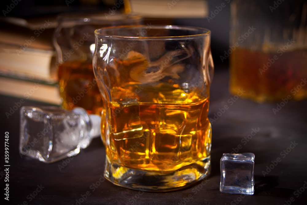 whiskey with ice on a wooden table. Nearby old books.