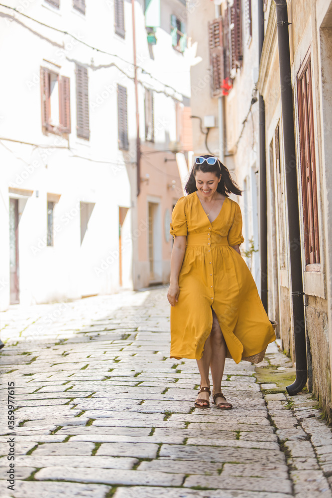 woman in yellow dress with bit straw hat walking by old tourist city in croatia
