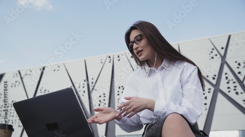 Fotografie Young caucasian business woman with long hair talk on skype using laptop sitting outdoor