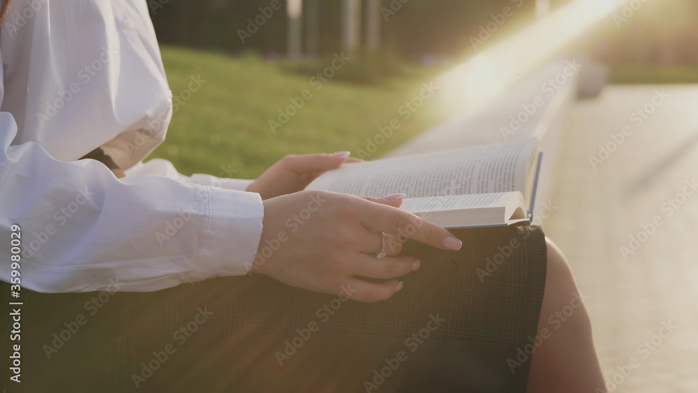Young woman sitting on the bench in a park and reading a book.
