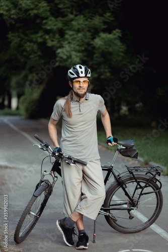 Fototapeta Naklejka Na Ścianę i Meble -  Attractive stylish man posing next to his bicycle on the park. He is holding his bicycle. High quality photo