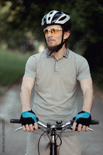 Cyclist in sportswear and helmet stands on the road in the park and looks to the side. High quality photo