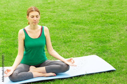 A woman practices yoga outdoors on the grass. Copy space