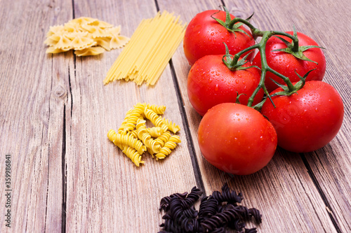 Tomatoes and different pasta on a wooden background