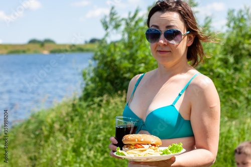 beautiful girl in a blue bathing suit with a plate of hamburgers and potatoes with a glass of Pepsi