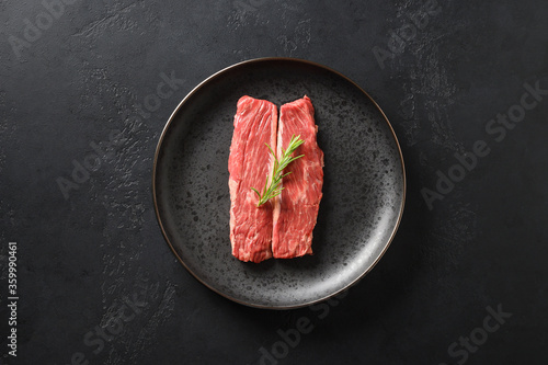 Raw ribeye steak with rosemary on black background. Minimal style. View from above. photo