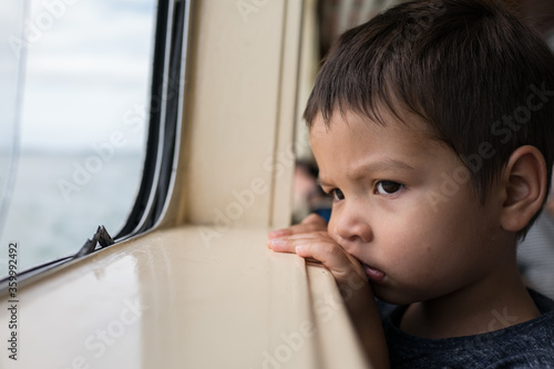 Cute 3 year old mixed race boy looks out a boat window photo