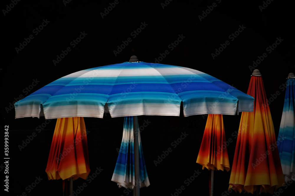 Colored beach umbrellas, vivid colors in contrast with the black background.