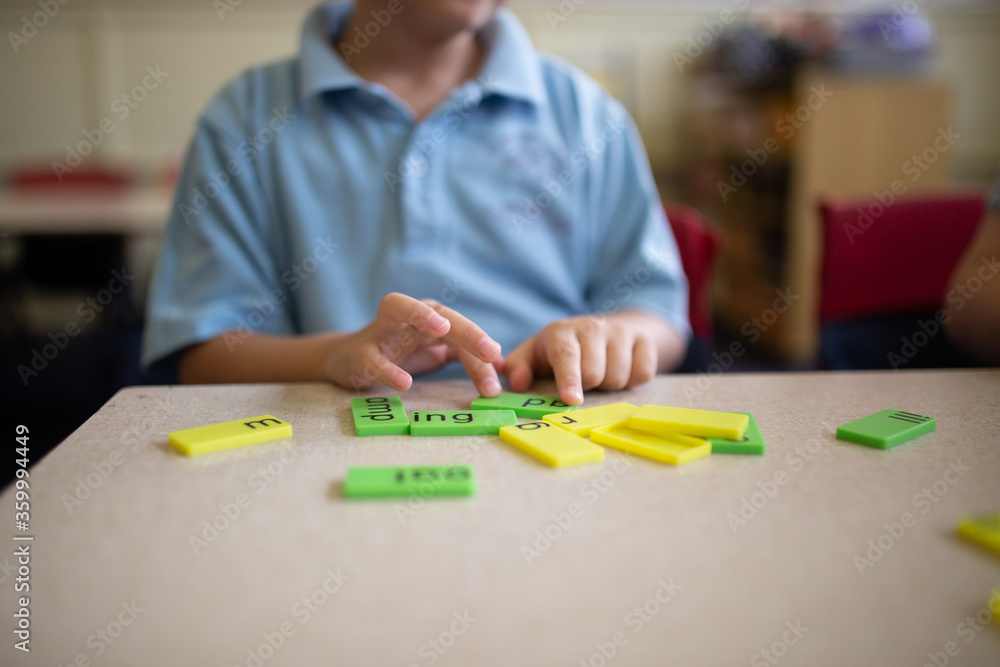 Closeup of primary school student's hands working with green and yellow word tiles Closeup of primary school student's hands working with green and yellow word tiles