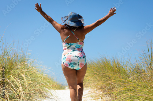 woman walking on dune path with arms raised in exultation photo