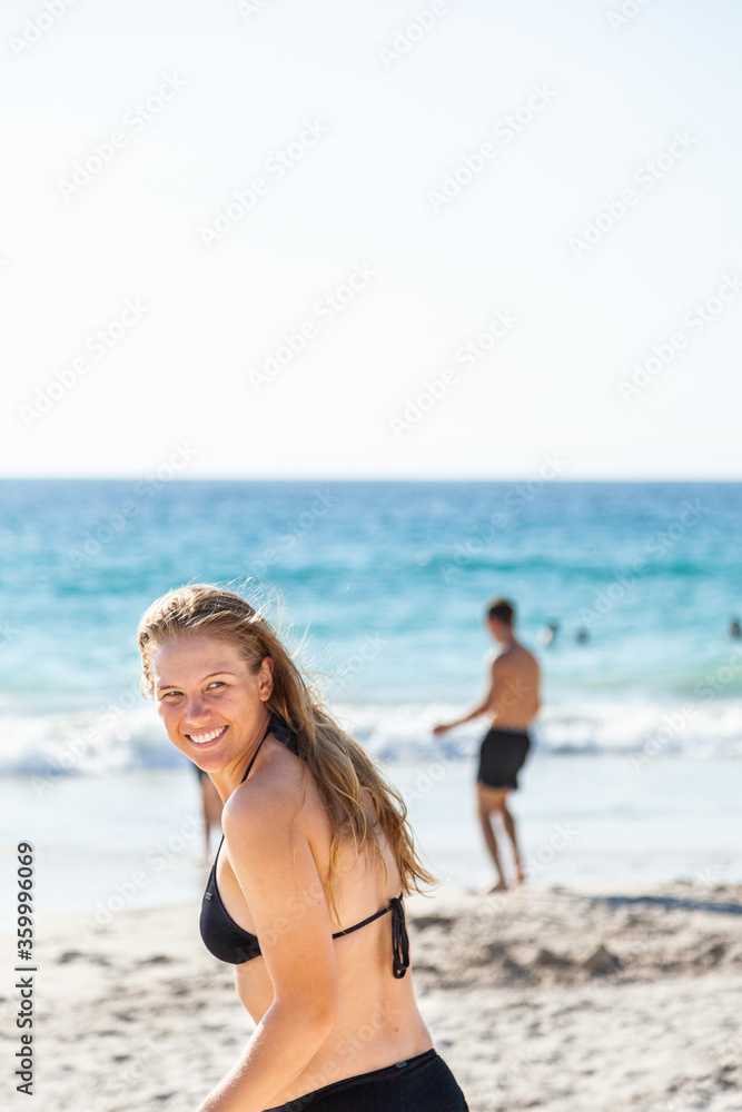 Happy young adult woman looking over her shoulder as she runs down to the sea at the beach Happy young adult woman looking over her shoulder as she runs down to the sea at the beach