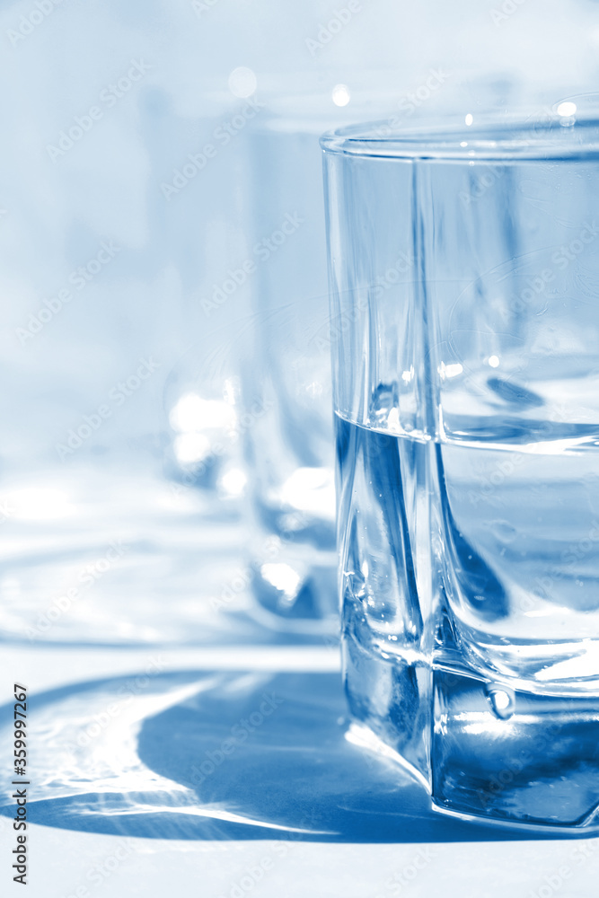 Sunshine through glass of water on background blue color, glare of glass, glass of water, glass of water