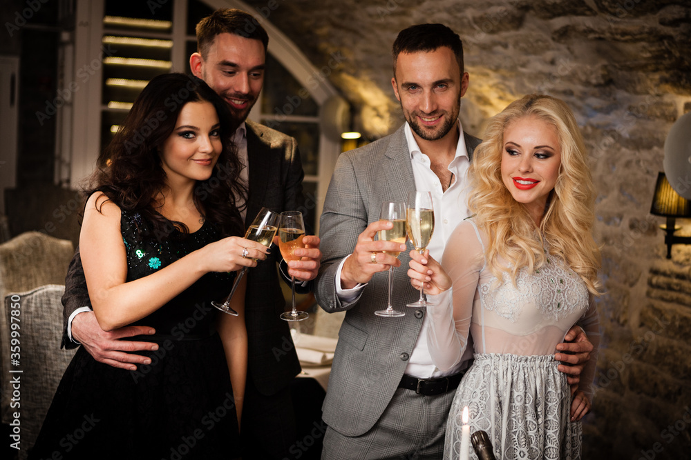 Party, holiday with friends concept. Four people with champagne glasses celebrating and toasting in restaurant. Two men and two women in elegant evening clothes, suits and dresses night out indoors