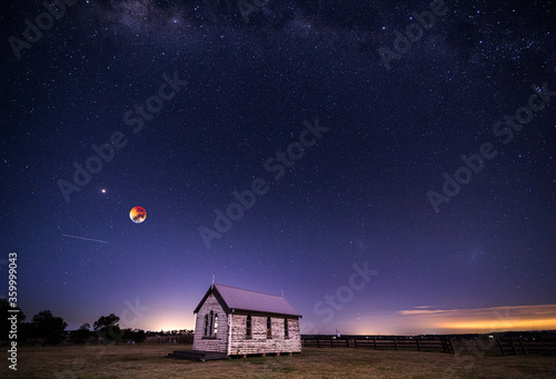 Blood moon setting, planet mars and a universe of stars shining brightly above the rustic chapel photo