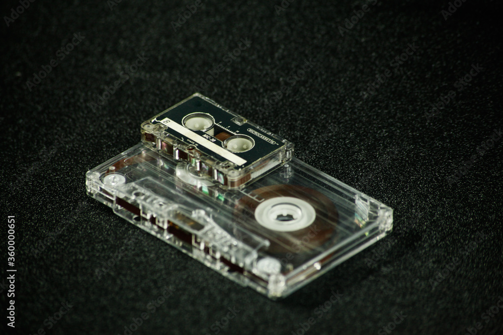 the microcassette and audio cassette are on a dark background the microcassette and audio cassette are on a dark background