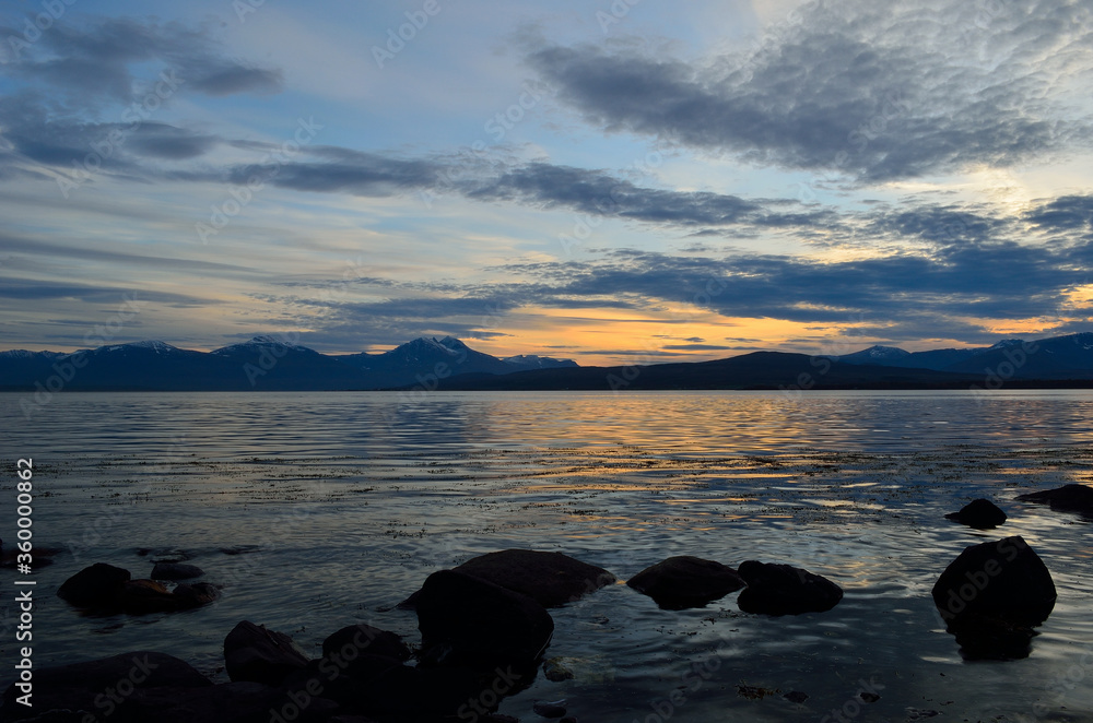 orange dawn sky over majestic mountain with new snow and reflection in the cold fjord water in late autumn