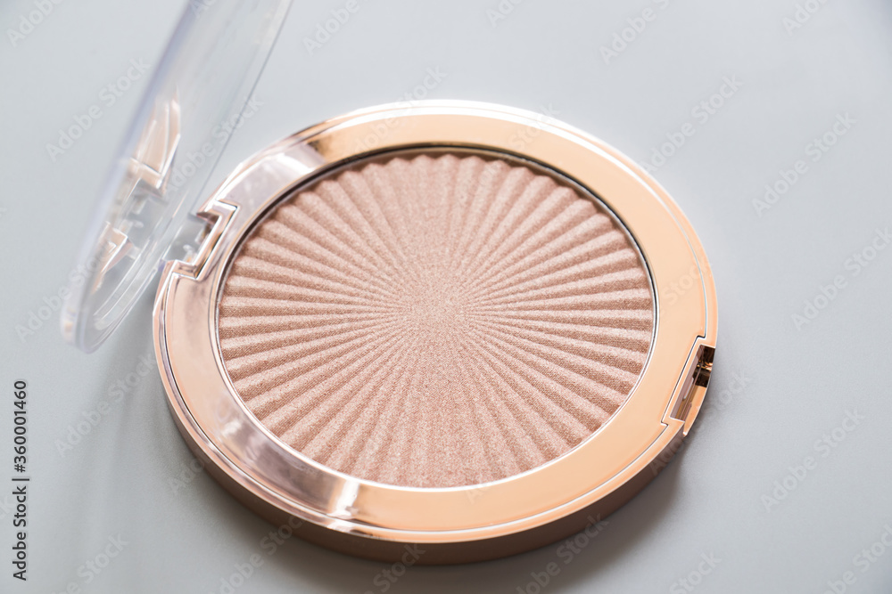 Highlighter, bronzer, cosmetic, makeup, gold, light. Highlighter for makeup on a grey background