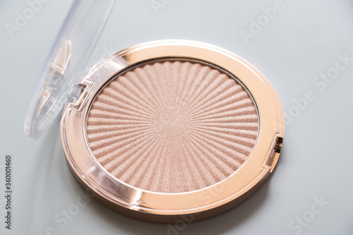 Highlighter, bronzer, cosmetic, makeup, gold, light. Highlighter for makeup on a grey background. Macro photography of highlighter for makeup on a grey background.