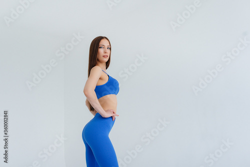 Sexy young girl posing in a blue tracksuit on a white background. Fitness, healthy lifestyle