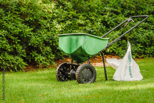 Fotografie Manual walk behind grass seed spreader and bag of lawn fertilizer in a green residential backyard