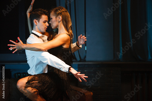 Dance and love concept. Young couple in elegant evening dresses posing in the room filled with dramatic light. Two dancers man and woman holding each other in passionate pose © Maksim Toome