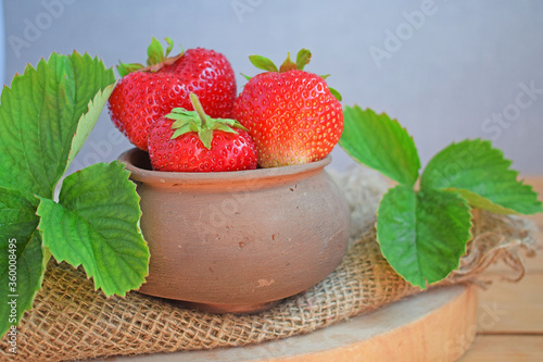 Fresh sweet strawberries in a clay pot on a wooden background.