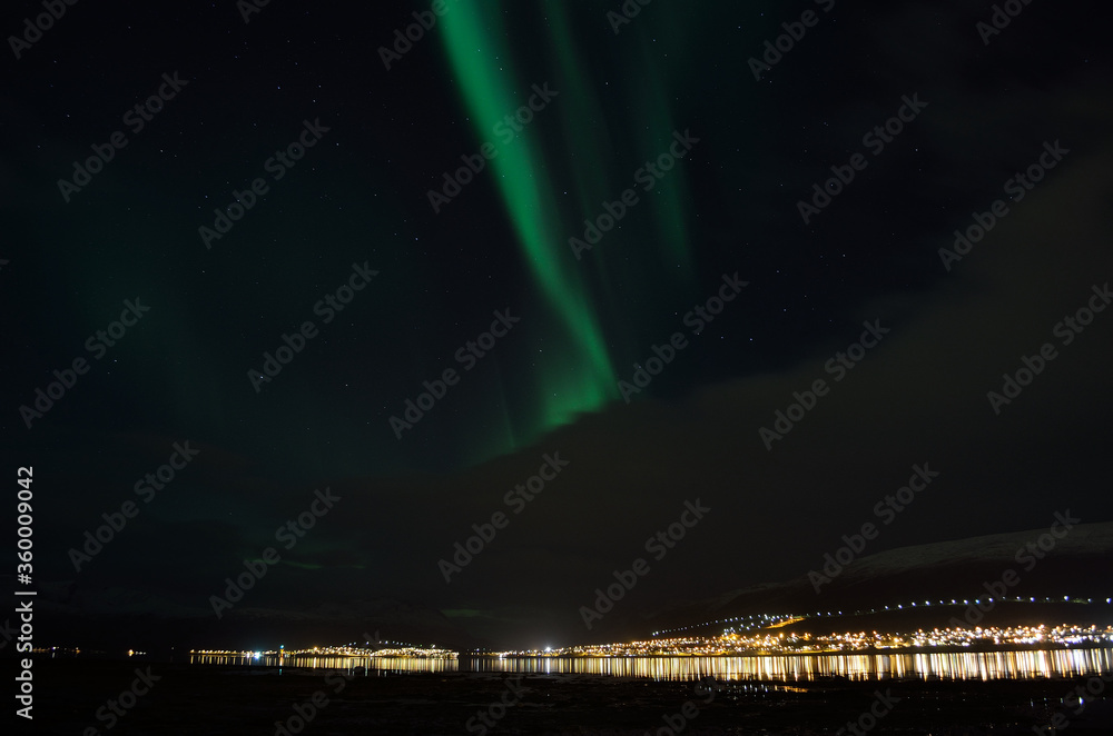aurora borealis, northern lights over mountain landscape with new snow reflecting on beach sand and fjord water illuminated by the whale island settlement lights in late autumn