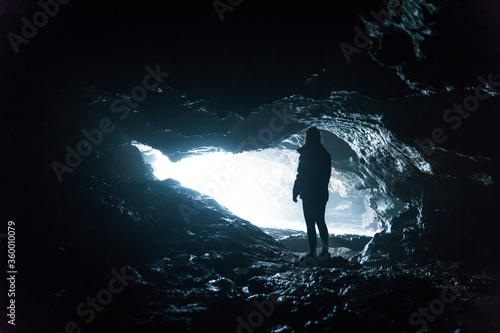 Silhouette of an explorer woman inside a cave next to the sea