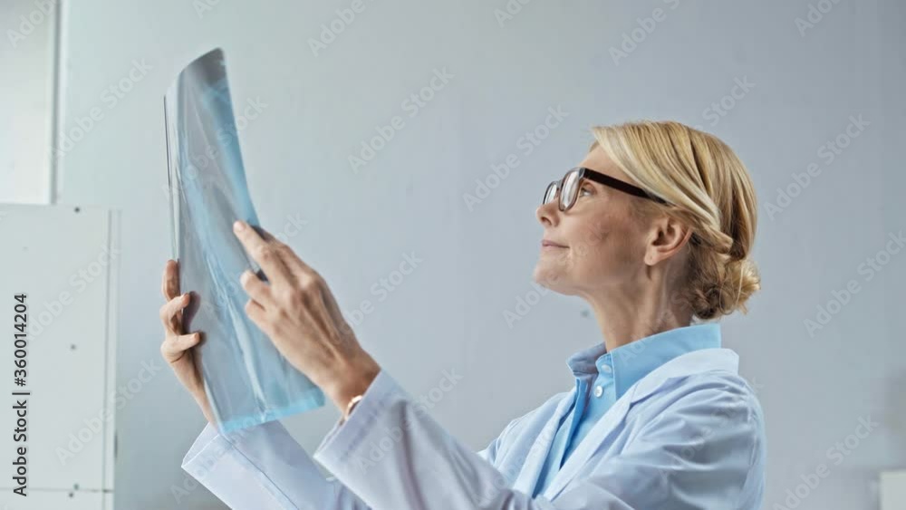 attractive middle aged doctor in glasses looking at x-ray attractive middle aged doctor in glasses looking at x-ray