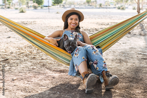 A woman sitting in a hammock with her french bulldog.