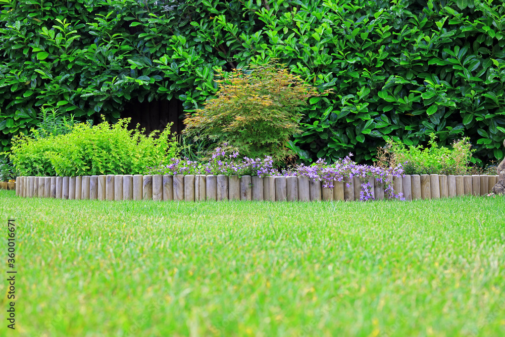 A wooden log roll edging between a grass lawn and a shrub border. - obrazy, fototapety, plakaty 