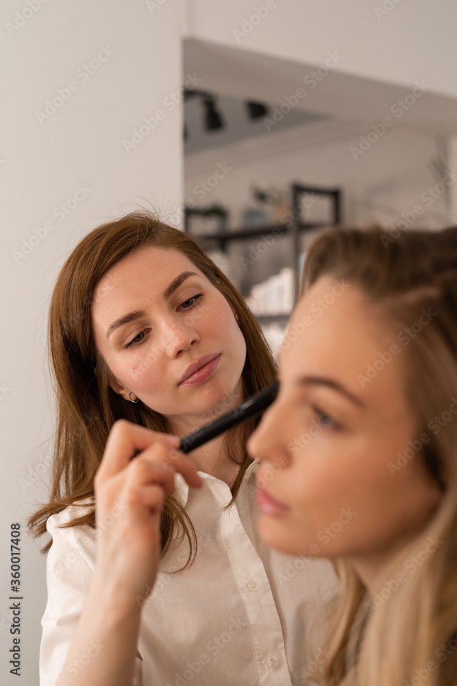 Young makeup artist applying powder on cheek of model Young makeup artist applying powder on cheek of model