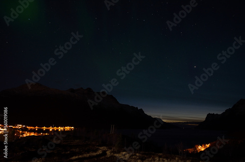 aurora borealis over mountain valley with fjord and settlement in the bottom