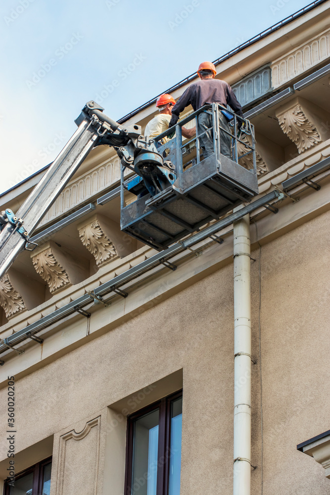 Reconstruction of the building of the Drama Theater in the city. Two working painters on an air platform paint a wall. Reconstruction of the building of the Drama Theater in the city. Two working painters on an air platform paint a wall.
