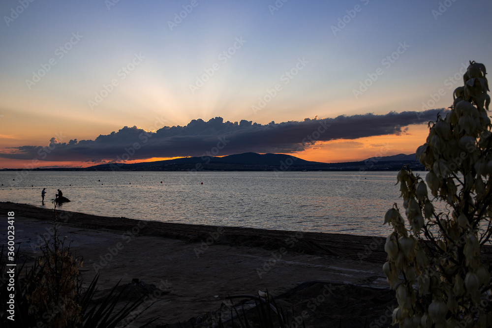 bright sea sunset in the resort city of Gelendzhik, the summer sun behind the clouds goes behind the mountains and the Bay. Black sea coast