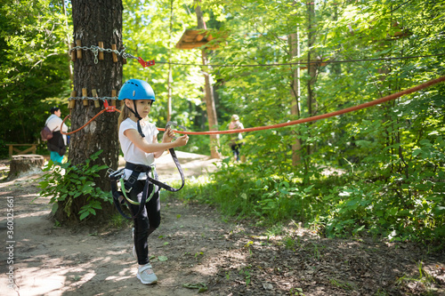 Rope adventure - a little girl with an insurance hook attached to the rope walking to the area