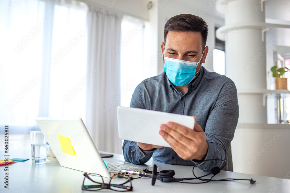 Mature businessman with mask using digital tablet at work. Male employee wearing a health mask Preventing corona virus infection covid-19, concept of working from home and social distancing Mature businessman with mask using digital tablet at work. Male employee wearing a health mask Preventing corona virus infection covid-19, concept of working from home and social distancing