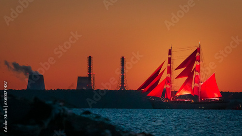 A ship with red sails at sunset on the background of a beautiful orange sky.