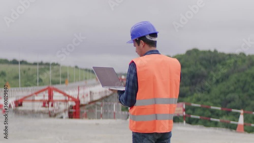 Construction engineer or an architect with a halmet and protective equipment on a building construction site using a laptop. photo