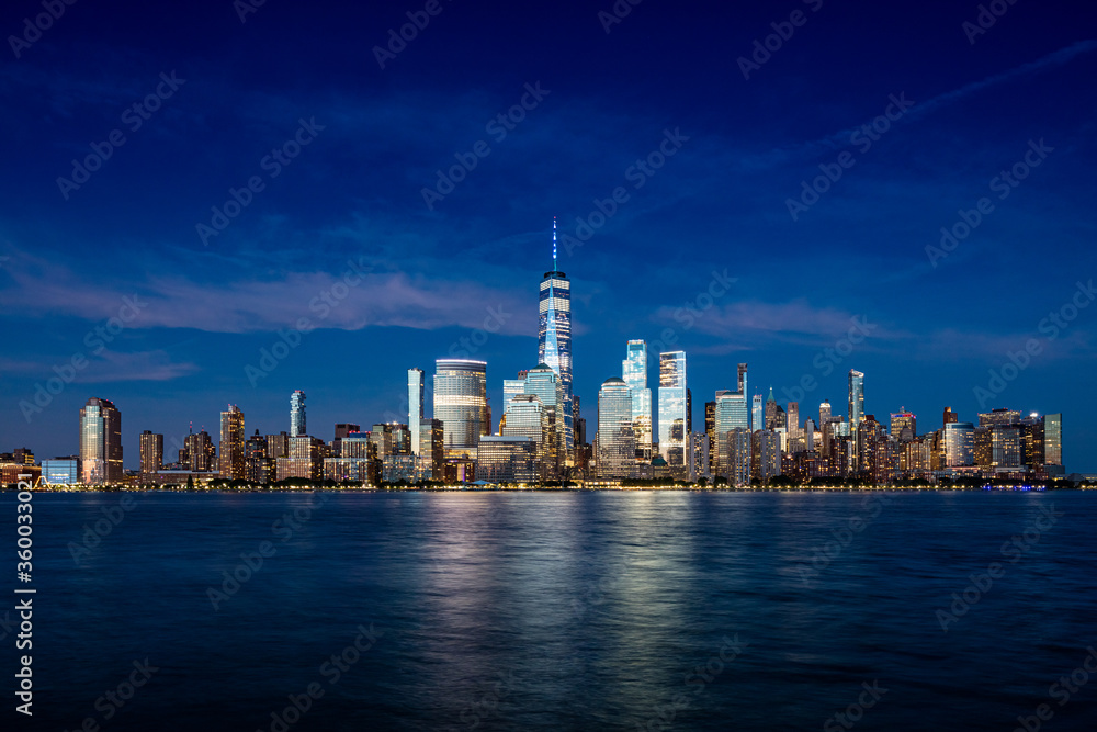 Downtown Manhattan skyline with light cirrus clouds at late blue hour as seen across the Hudson river from Exchange Place in Jersey City, New Jersey on June 21, 2020.