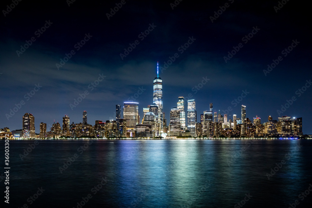 Fototapeta premium Downtown Manhattan skyline with light cirrus clouds at teal hour of the night as seen across the Hudson river from Exchange Place in Jersey City, New Jersey on June 21, 2020.