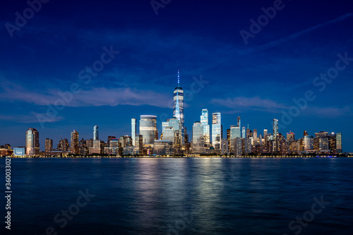 Downtown Manhattan skyline with light cirrus clouds at late blue hour as seen across the Hudson river from Exchange Place in Jersey City, New Jersey on June 21, 2020.