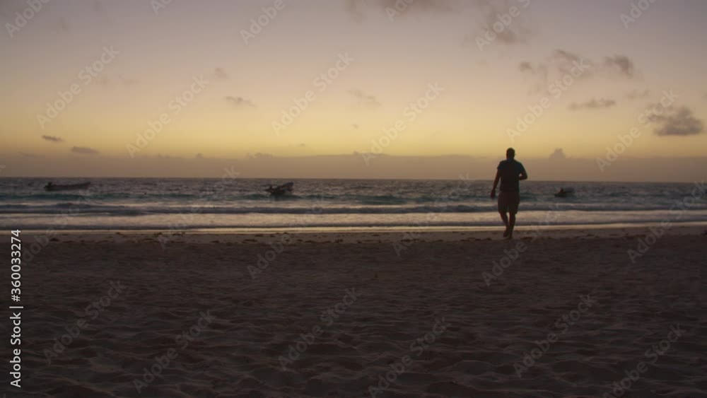 A photographer walking to the shore and taking a picture near the water in the beach while sunrise A photographer walking to the shore and taking a picture near the water in the beach while sunrise
