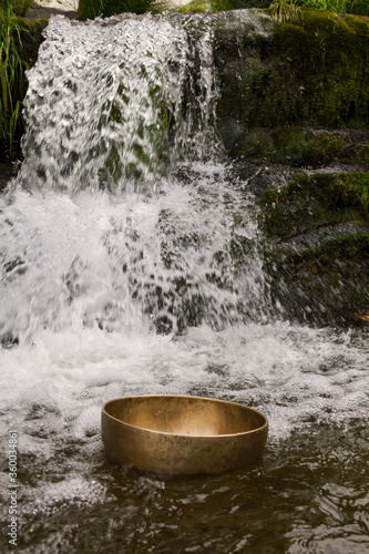 Tibetan singing bowl floating in the water with waterfall in the background.