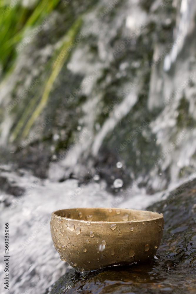 Vertical view of tibetan singing bowl floating in the water with small waterfall in the background.