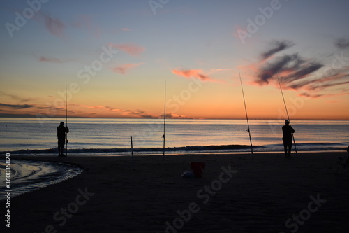 Sports fishermen with fishing rods at the beach of Katwijk aan Zee in the evening at sun set 