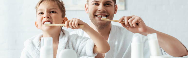 selective focus of happy father and son brushing teeth together, panoramic shot