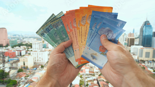 Canvas Print A young man recounts in his hands the money of Malaysia against the background of the city center of Kuala Lumpur