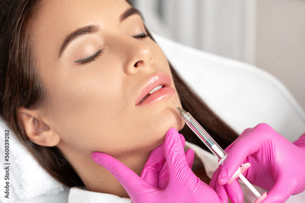 Woman with beautiful clean skin. Cosmetologist does injections for lips augmentation and anti wrinkle in the nasolabial folds of a beautiful woman. Women's cosmetology in the beauty salon.